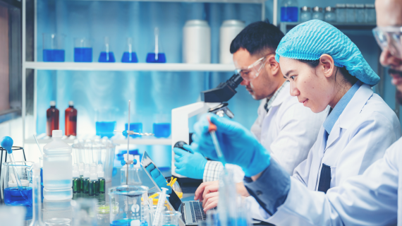 People in a lab working with a microscope, droppers and test tubes.
